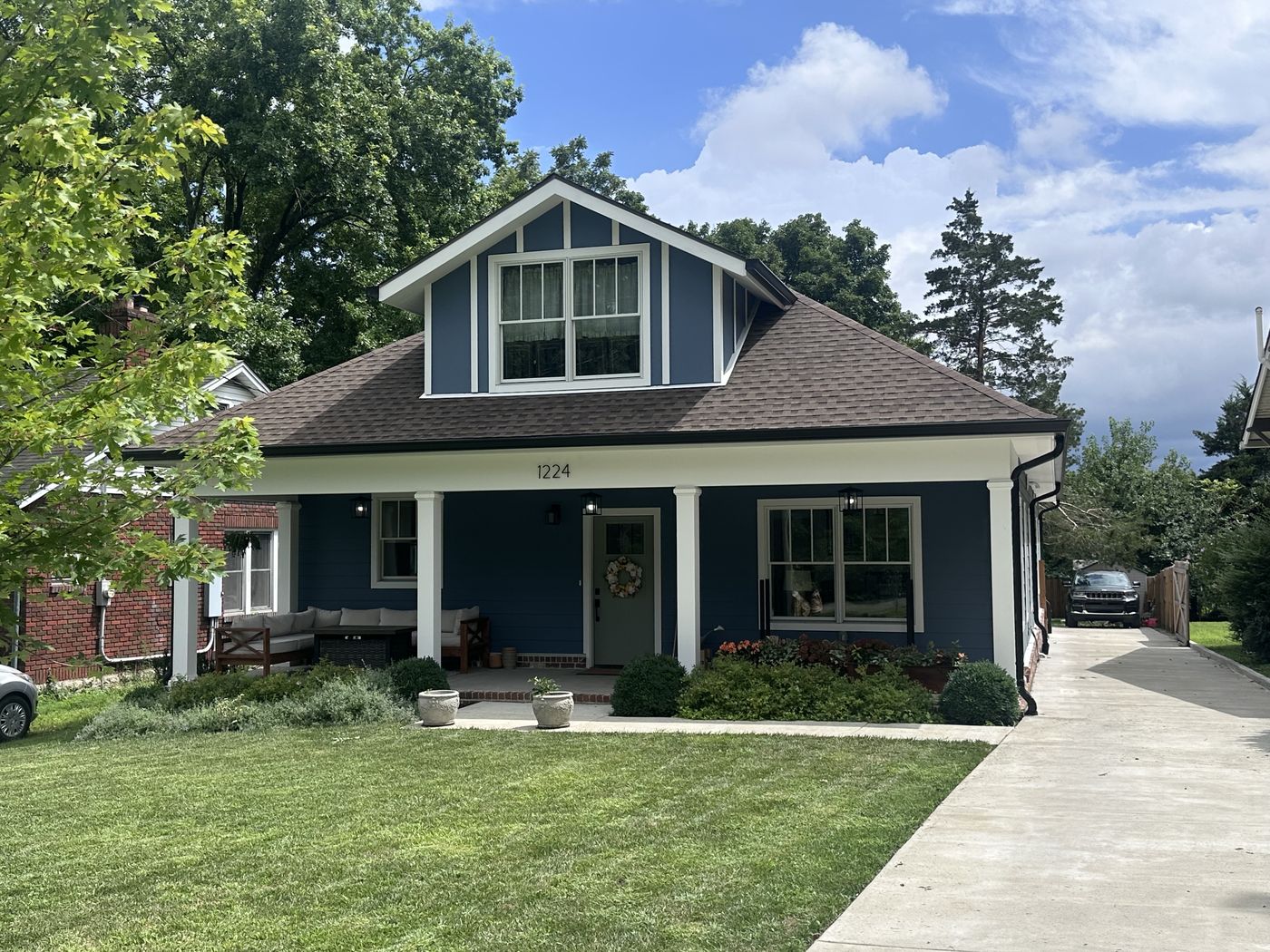 The house at 1224 Howard Avenue — a blue home with a white columned front porch, flower beds, and a green lawn.